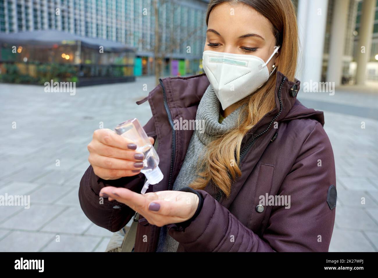 Donna con KN95 FFP2 maschera utilizzando gel di alcol sanitizzante le mani in città strada Foto Stock