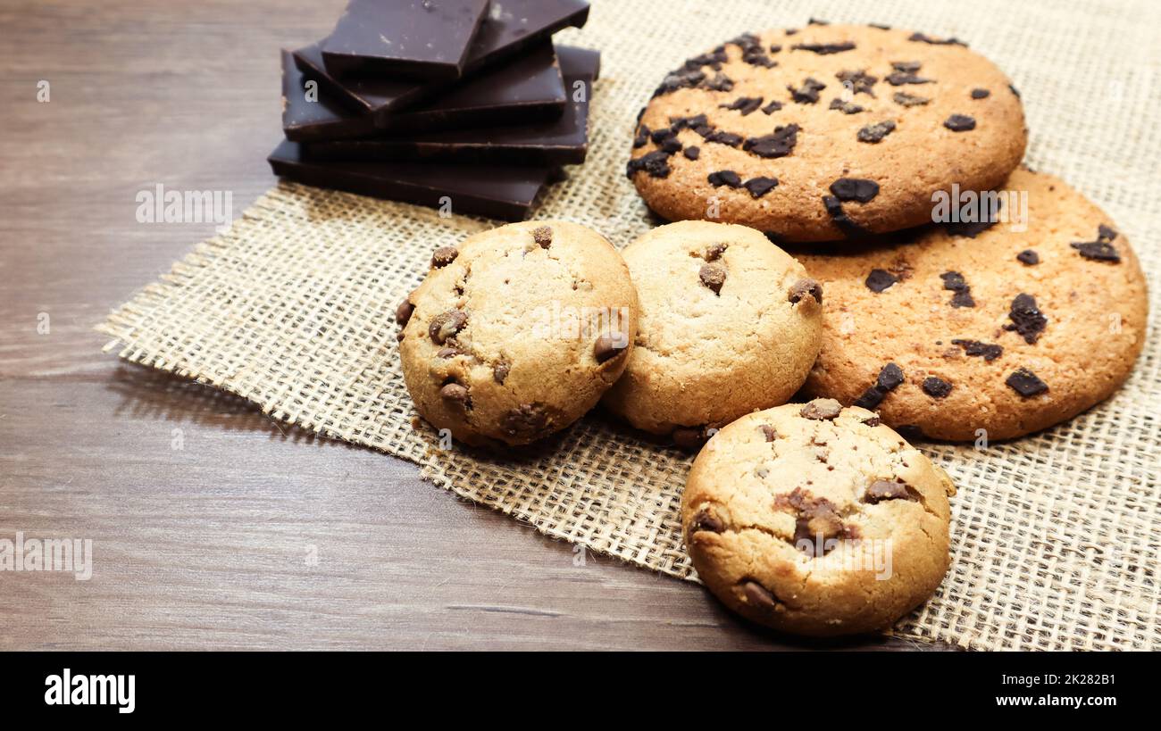 Biscotti al cioccolato americano su un tavolo di legno marrone e su un primo piano di tovagliolo di lino. Tradizionale impasto croccante arrotondato con gocce di cioccolato. Panetteria. Delizioso dessert, dolci. Vita ferma rurale. Foto Stock