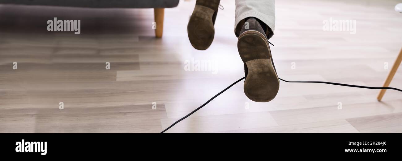 Gambe dell'uomo che inciampano con un cavo elettrico Foto Stock