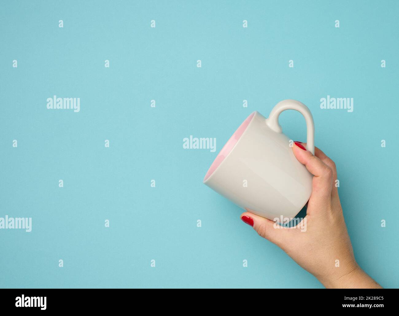 la mano femminile tiene una tazza di ceramica su sfondo blu, il tempo di pausa e bere caffè Foto Stock
