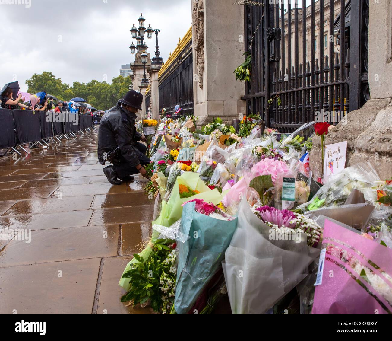 Londra, Regno Unito - Settembre 9th 2022: Un poliziotto che mette fiori davanti alle porte di Buckingham Palace a Londra, in commemorazione della Regina Elisabetta Foto Stock