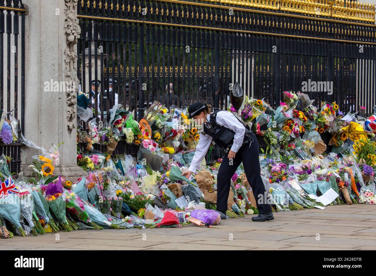Londra, Regno Unito - Settembre 9th 2022: Un poliziotto che mette fiori davanti alle porte di Buckingham Palace a Londra, in memoria della Regina Elisabetta II, Foto Stock