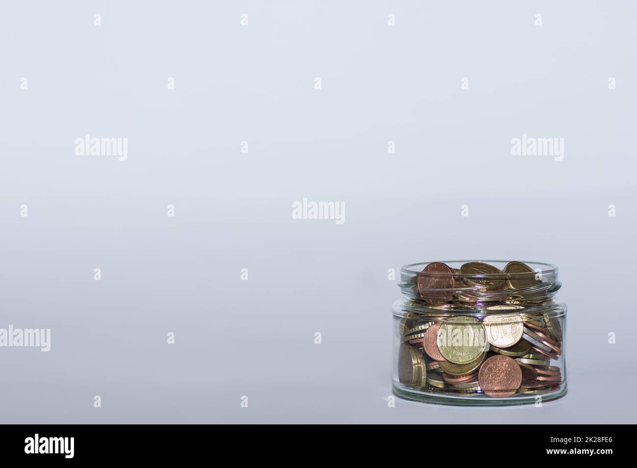 risparmio di denaro in un vetro piatto con molte monete in euro diverse per l'indipendenza finanziaria con grigio Foto Stock