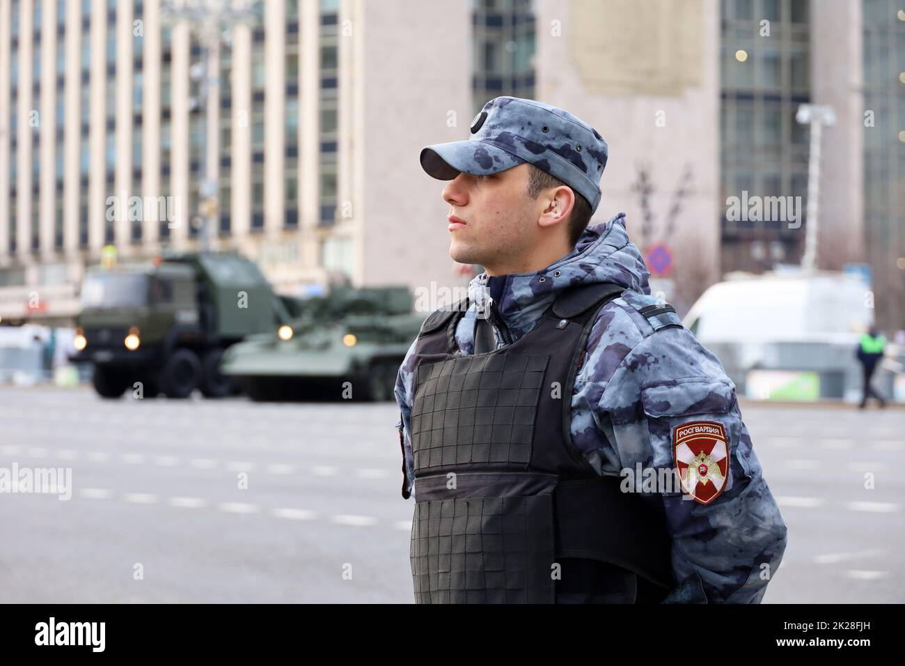 Soldato delle forze militari russe della Guardia Nazionale in giubbotto a prova di proiettile sullo sfondo di veicolo blindato su strada cittadina Foto Stock