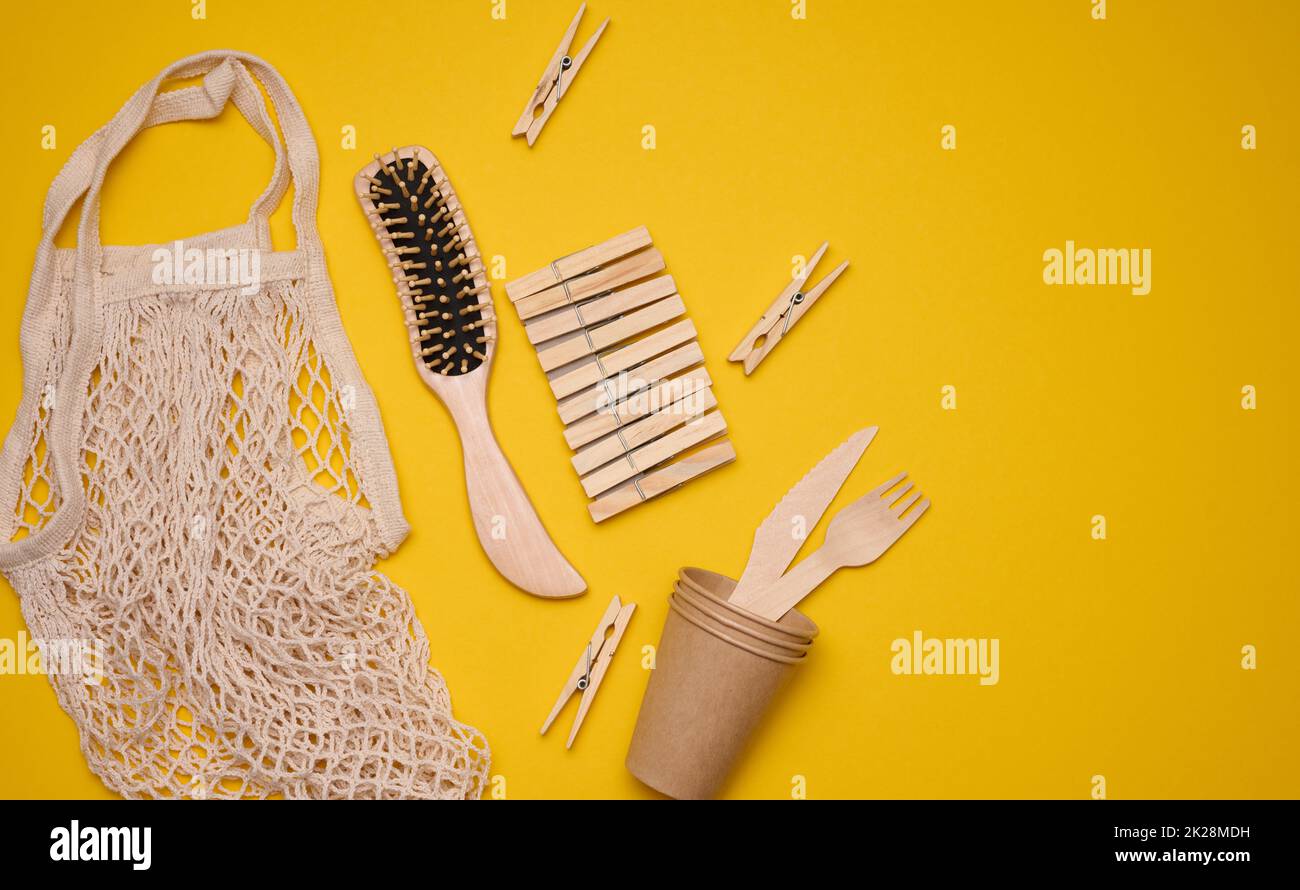 borsa di cotone bianco, tazze di carta e forchette e cucchiai di legno su sfondo giallo. Rifiuti riciclabili, vista dall'alto Foto Stock