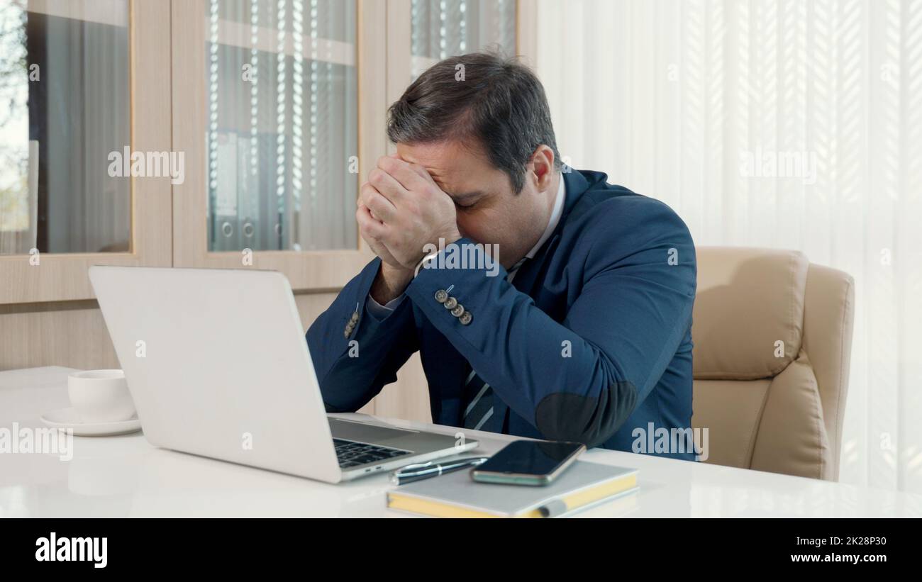 Un uomo d'affari stressato che si sente malato e stanco mentre si siede al suo posto di lavoro Foto Stock