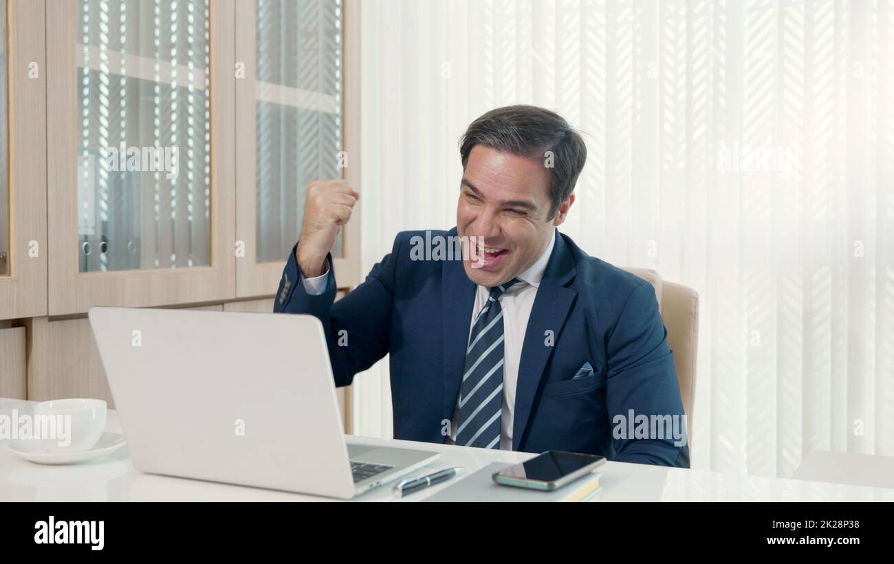 Uomo d'affari seduto utilizzando laptop studio lavoro online alla sua scrivania celebrazione di successo in ufficio Foto Stock