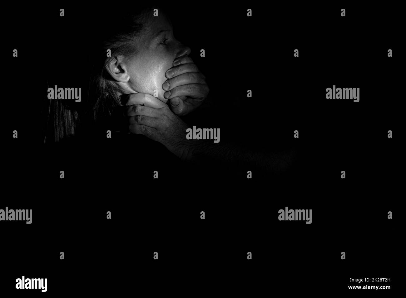 La mano di un uomo chiude la bocca e strangolare una ragazza al buio, violenza e paura, violenza contro una donna, un assassino Foto Stock