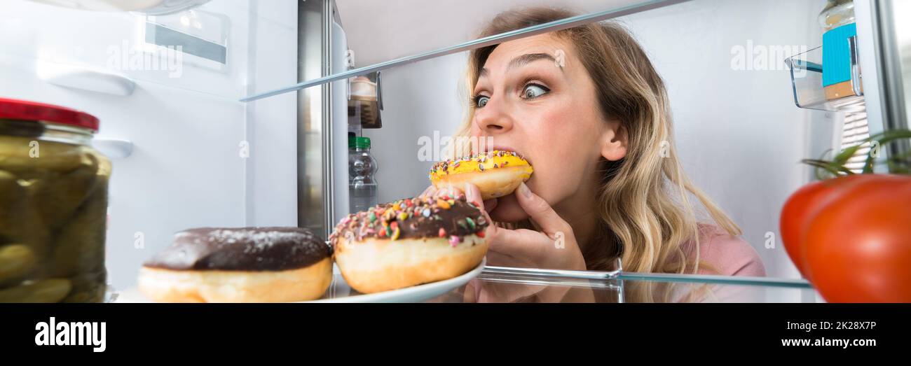 Donna affamata che mangia la torta dal frigorifero. Stile di vita malsano Foto Stock