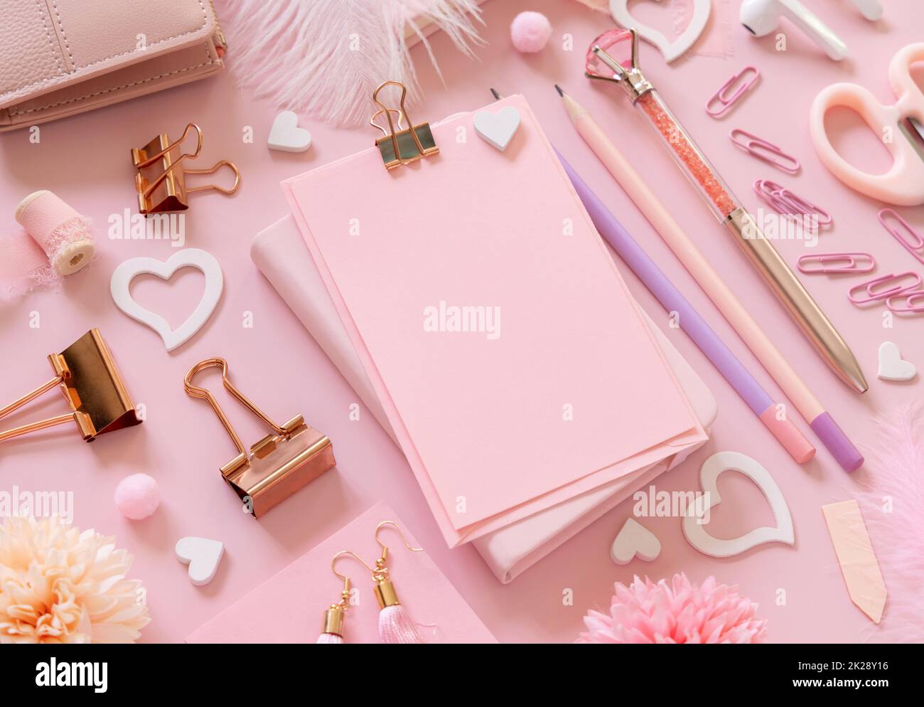Cartoncino di carta rosa con clip, accessori da scuola girly e cuori su rosa pastello primo piano, mockup Foto Stock