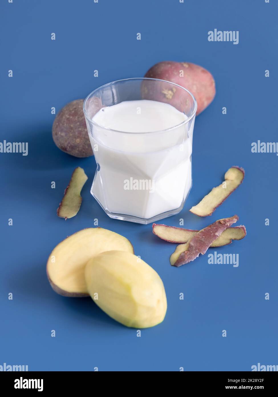 Bicchiere di latte di patate vegetale su tavola blu vicino ai tuberi di patate Foto Stock