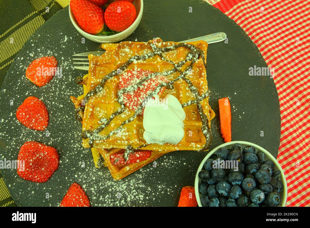 Waffle belgi fatti in casa con mirtilli e fragole su sfondo ardesia. Cioccolato fuso su cialde. Design piatto Foto Stock