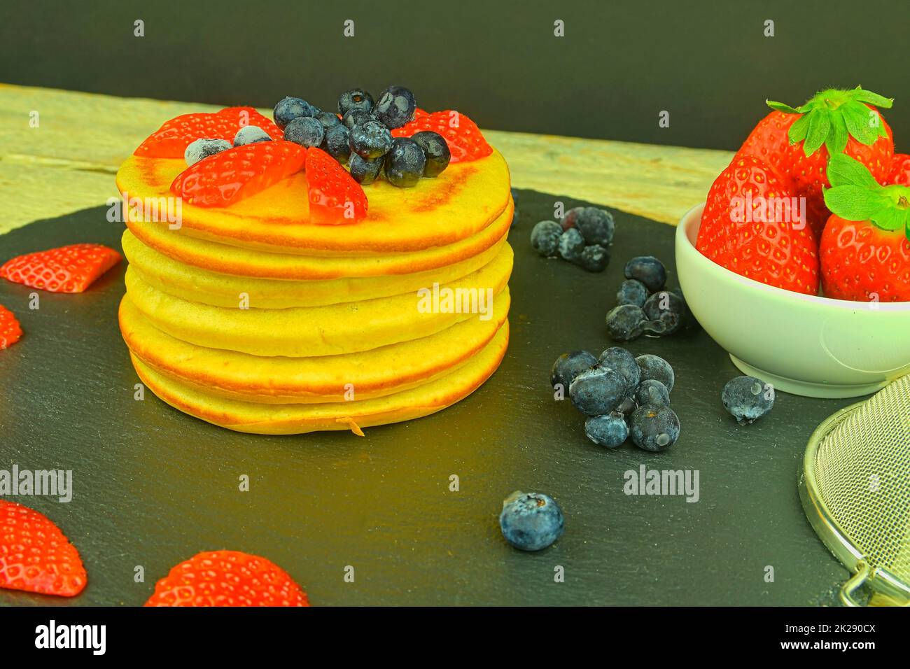 Una pila di pancake fatti in casa per colazione. Mirtilli e fragole su pancake. Sfondo nero, vista dall'alto Foto Stock