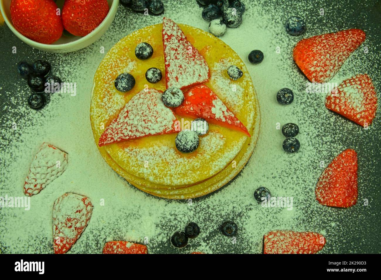 Pancake con frutti di bosco su sfondo nero. Pancake freschi. Mirtilli, fragole e zucchero a velo sui pancake. Disposizione piatta Foto Stock