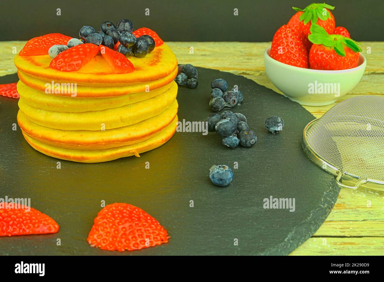 Una pila di pancake fatti in casa per colazione. Mirtilli e fragole su pancake. Sfondo nero, vista dall'alto Foto Stock