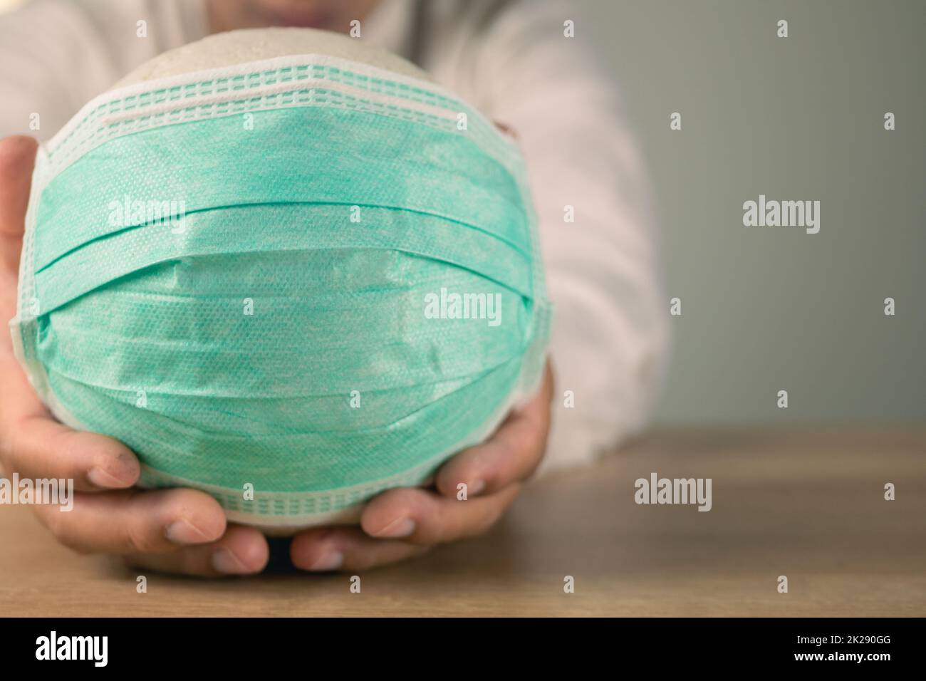Assicurazione sanitaria in concetto COVID. Un uomo tiene una palla bianca con maschera medica verde. Primo piano medio con spazio di copia. Foto Stock