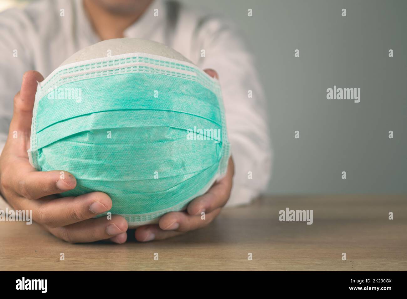 Assicurazione sanitaria in concetto COVID. Un uomo tiene una palla bianca con maschera medica verde. Primo piano medio con spazio di copia. Foto Stock