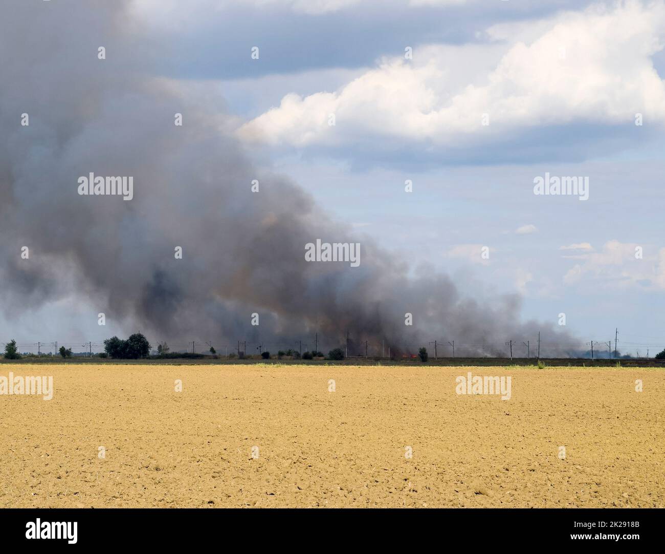 L'incendio è da qualche parte al di là del campo arato. Fumo scuro da un fuoco. Foto Stock