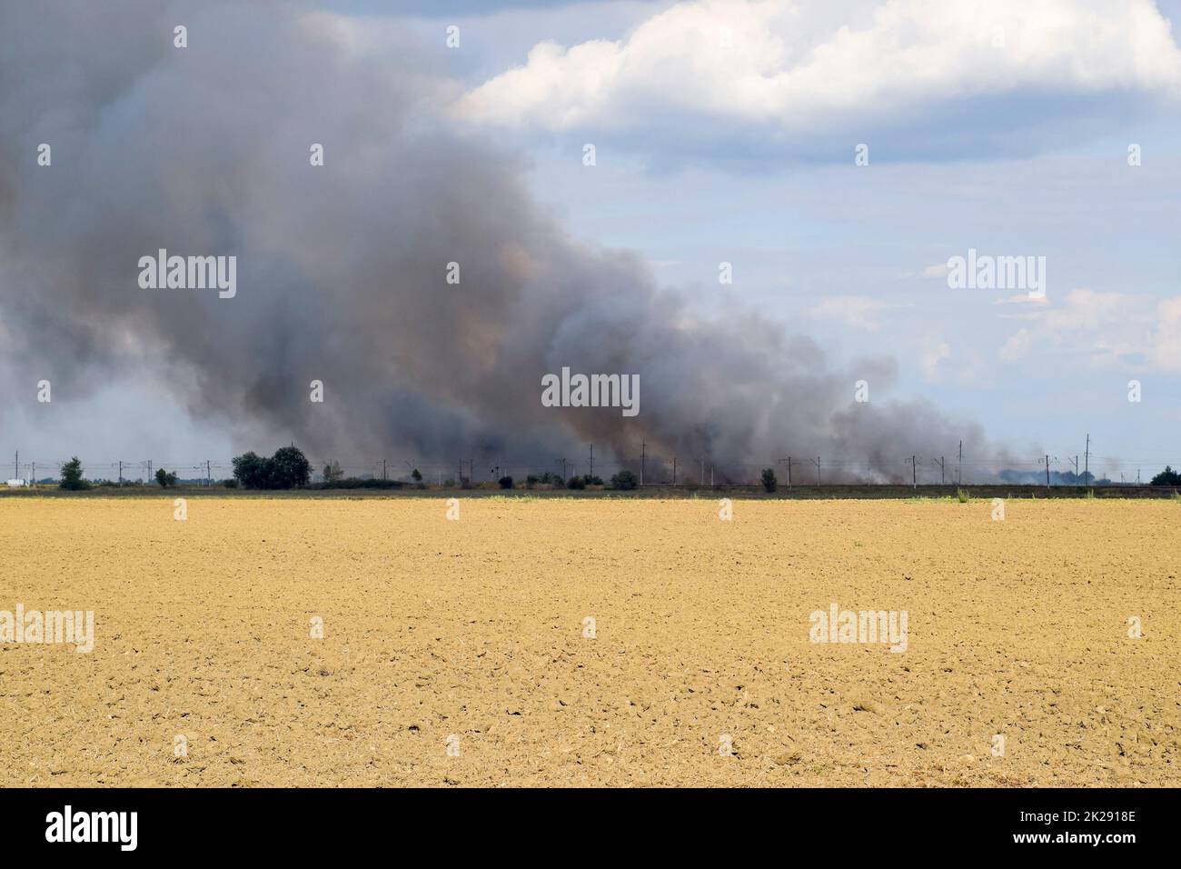 L'incendio è da qualche parte al di là del campo arato. Fumo scuro da un fuoco. Foto Stock