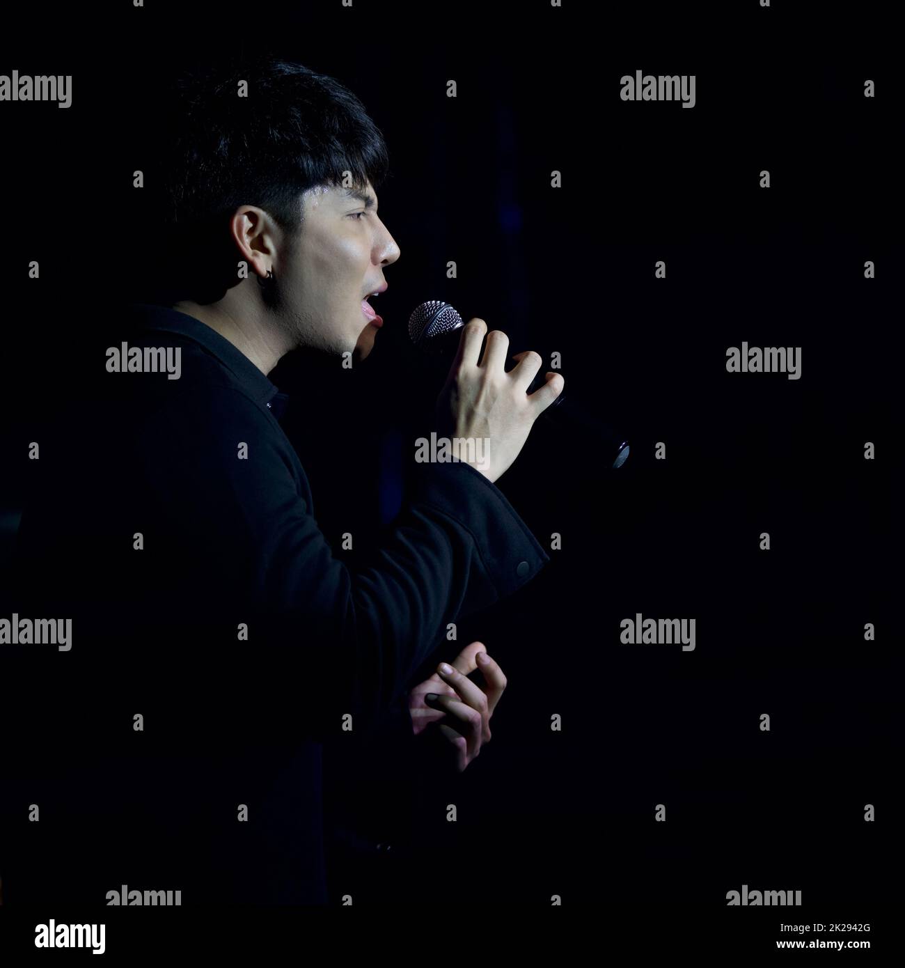 Giovane cantante asiatico dai capelli neri con un microfono che canta sul palco. L'atmosfera di notte nel pub Foto Stock