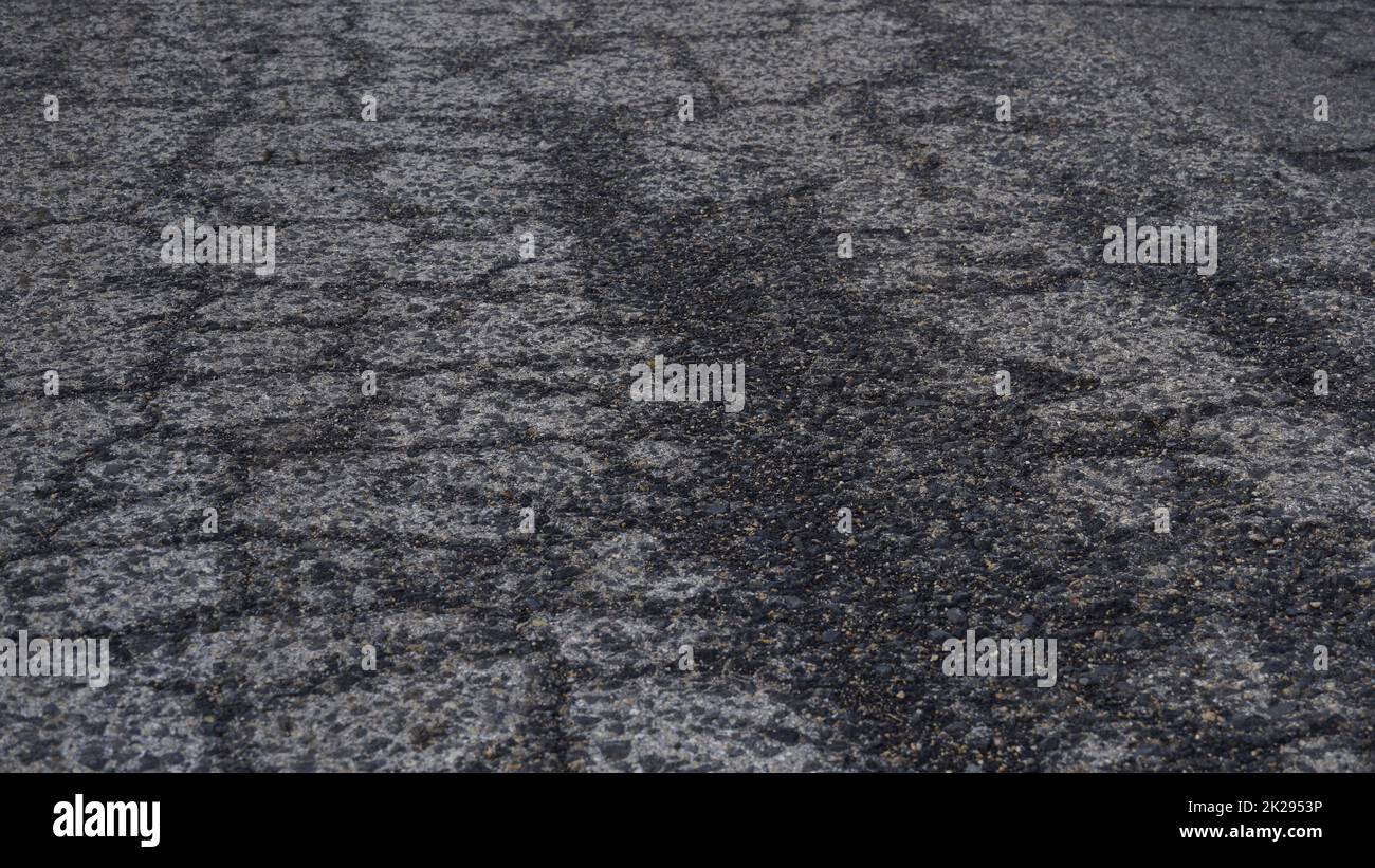 Vista ravvicinata di una vecchia strada asfaltata in presenza di crepe bagnate. Strada usurata con grana incrinata. Foto Stock