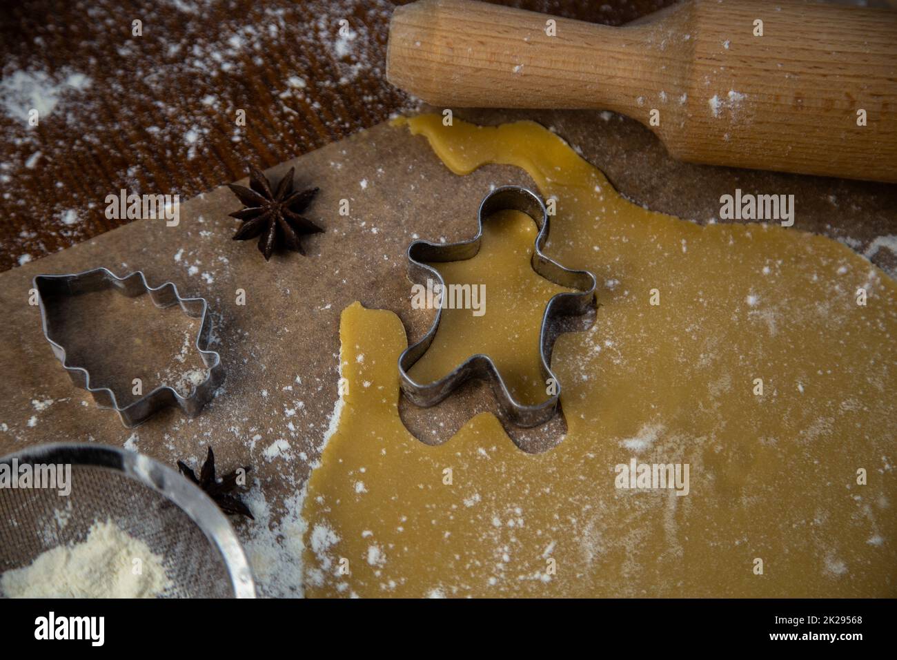 I biscotti sono tagliati fuori dalla pasta arrotolata nella forma di un uomo, la mano del pasticciere tiene una taglierina del biscotto Foto Stock