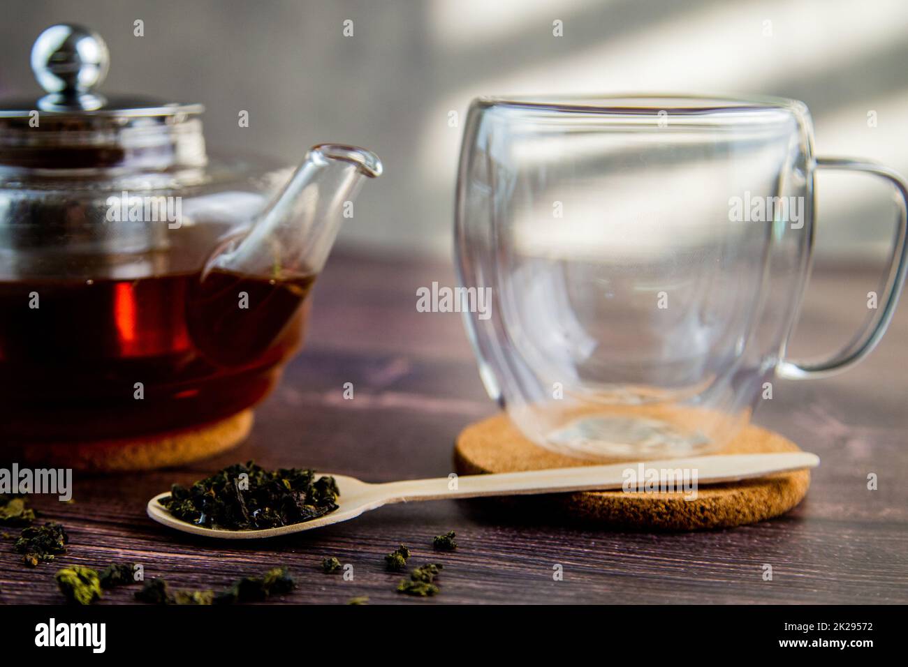 Un cucchiaio di legno con tè si trova su uno sfondo di legno scuro, una tazza e una teiera sono visibili da dietro, una foto in colori scuri. Foto Stock