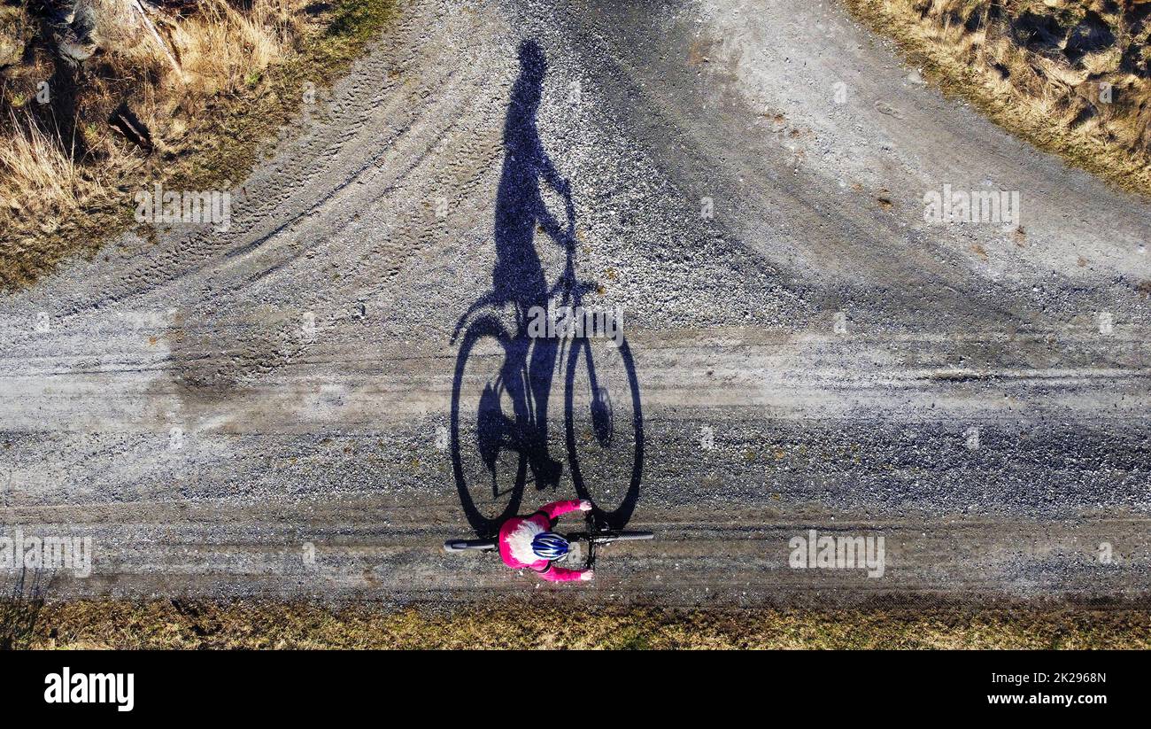Scatto aereo con drone di ciclista femminile su strada con ombra Foto Stock