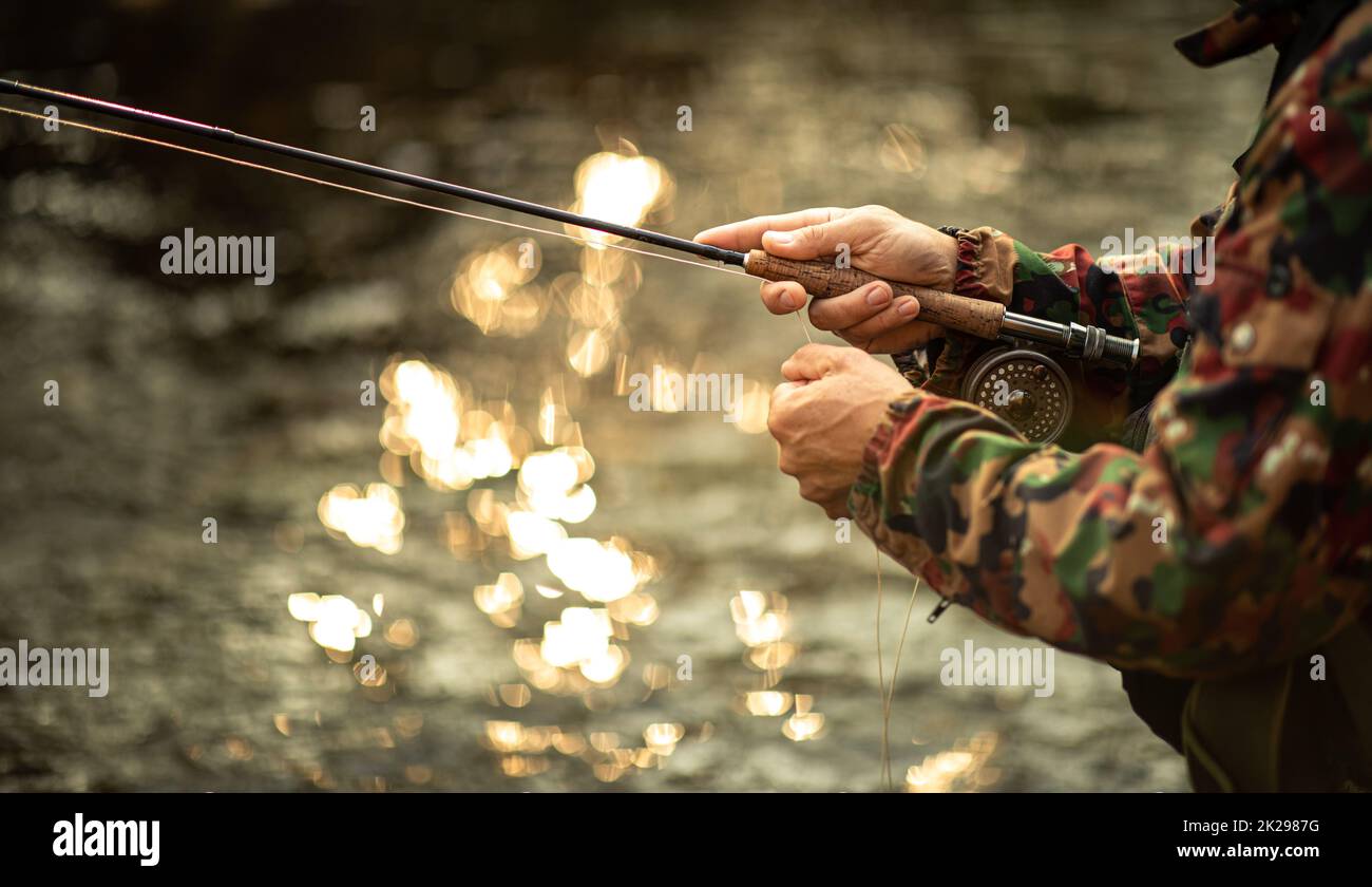 Vista ravvicinata delle mani di un pescatore a mosca che lavorano la linea e la canna da pesca mentre la pesca con la mosca su di uno splendido fiume di montagna per la trota iridea Foto Stock