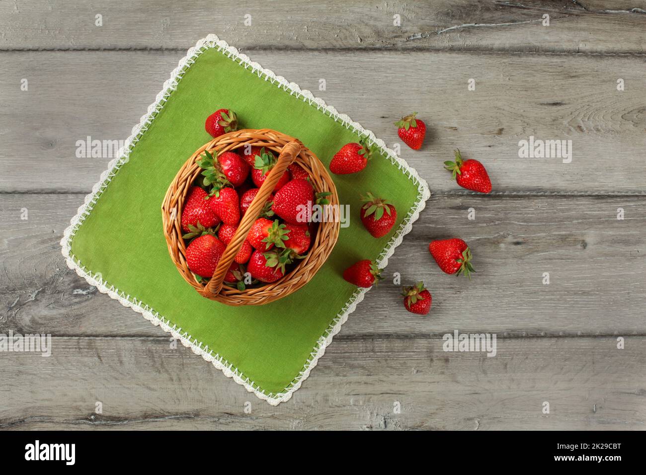 Vista del piano portapaziente, piccola cesta piena di fragole, alcuni di loro versato sul tavolo verde panno sotto di esso. Foto Stock