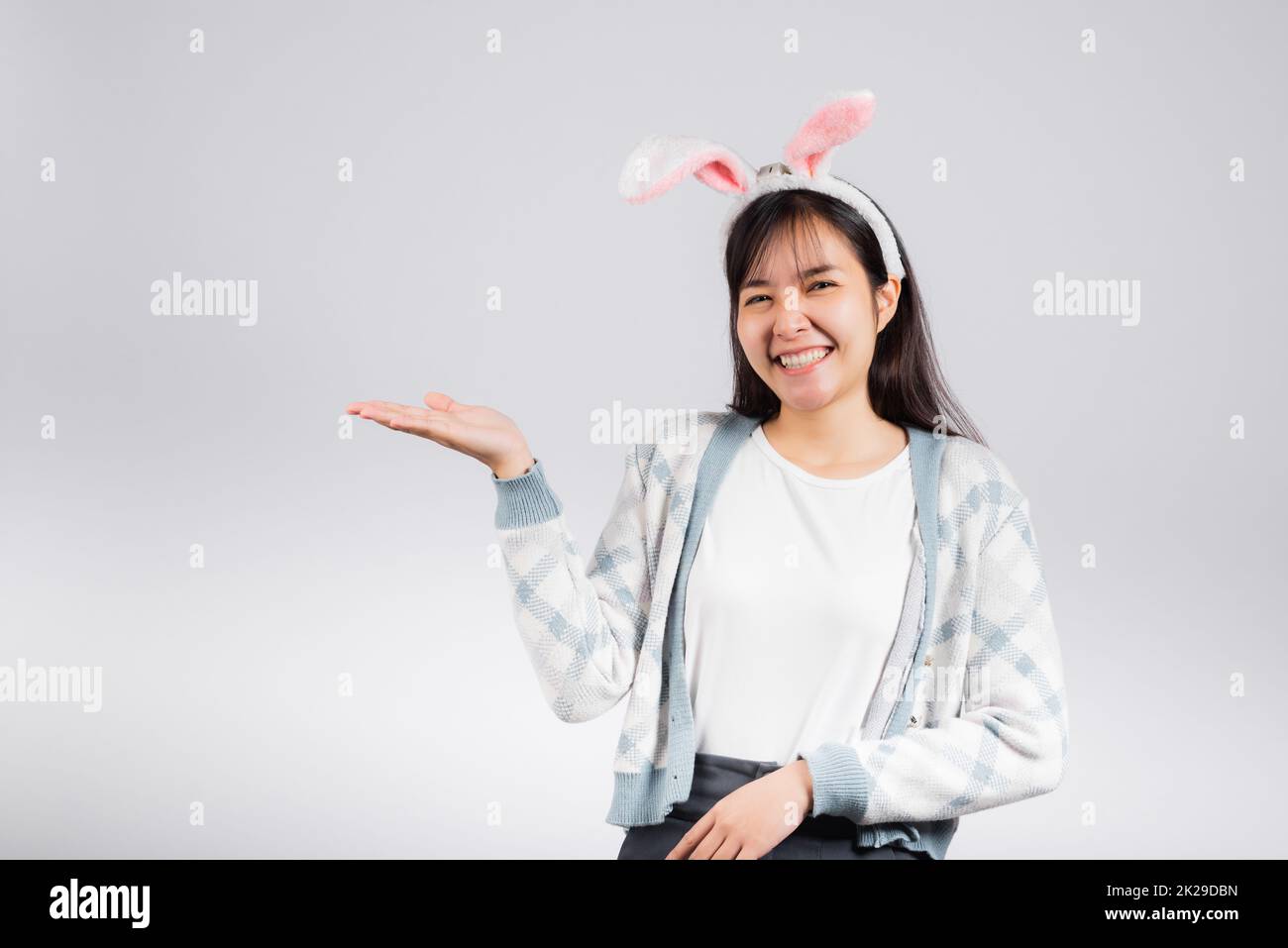 Concetto di Pasqua. Sorridente donna felice indossando orecchie di coniglio che presenta il prodotto tenendo qualcosa sul lato lontano della palma Foto Stock