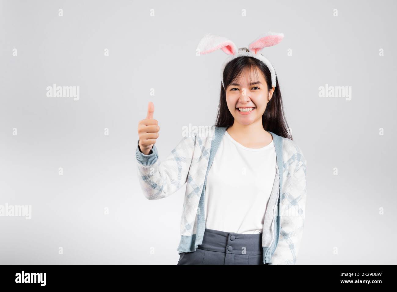 Sorridente donna felice che indossa le orecchie di coniglio mostra pollice in su per buon segno Foto Stock