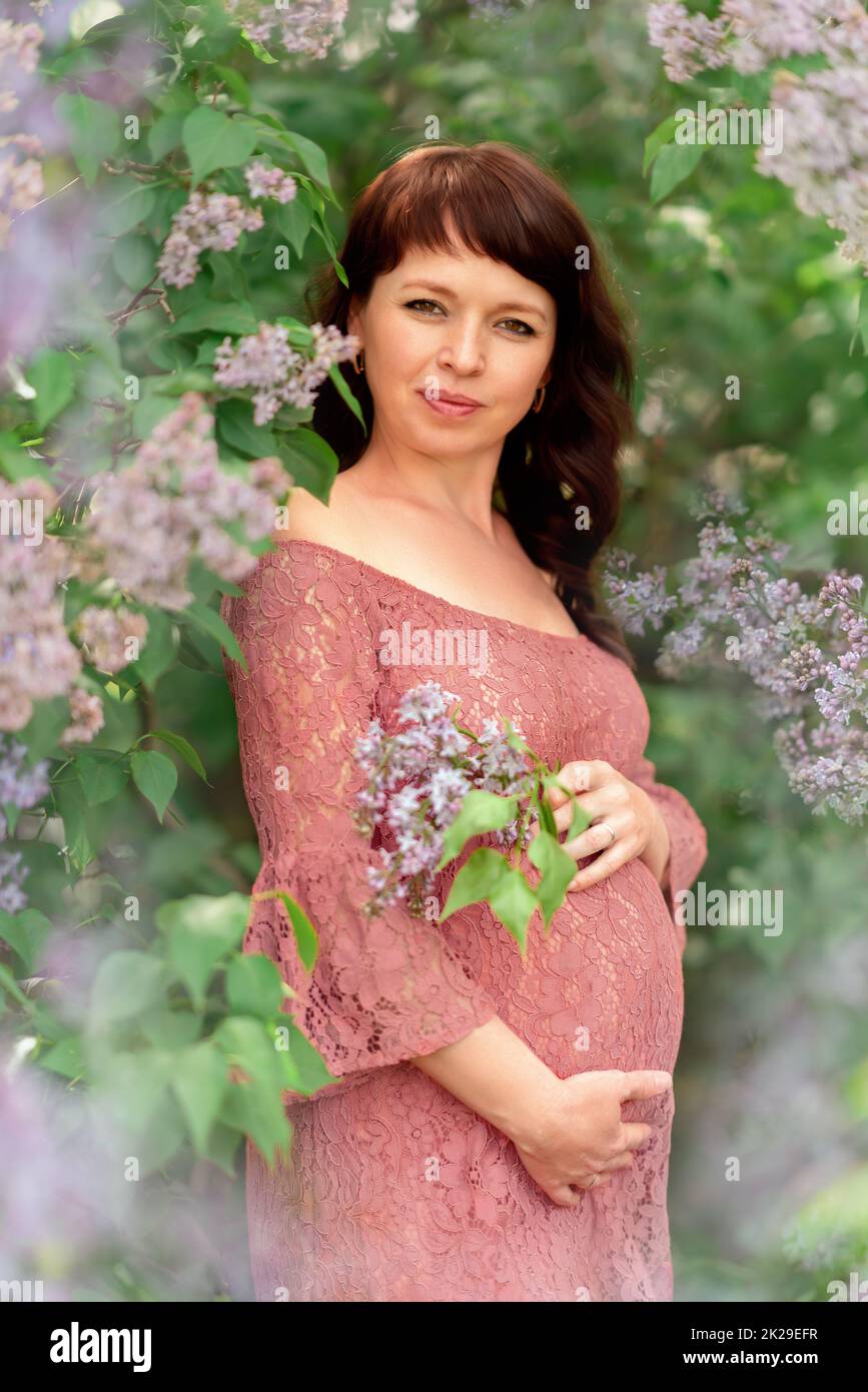 Una giovane donna incinta si erge nei cespugli lilla. Foto Stock