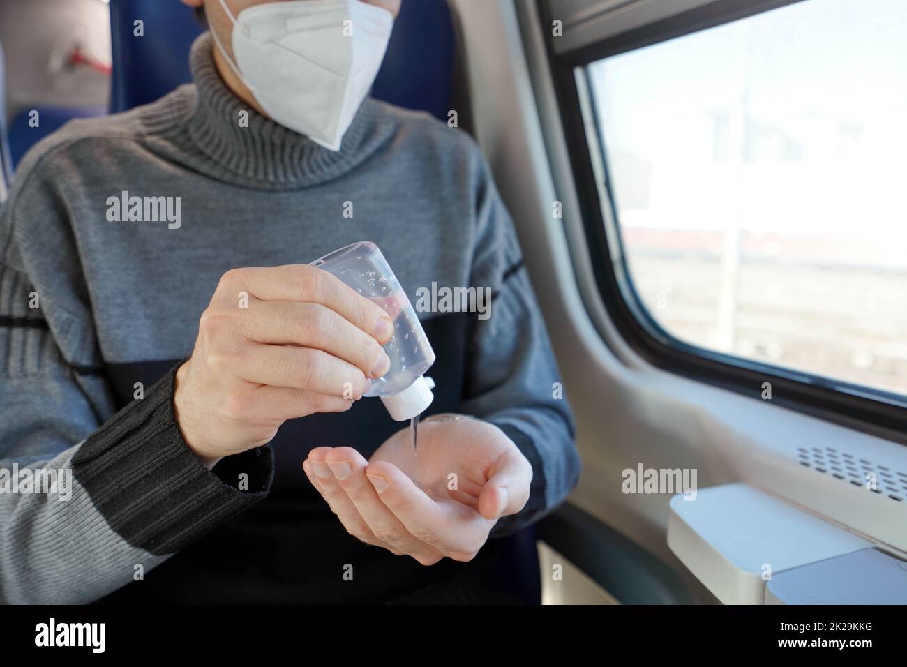 Viaggiare in sicurezza con i mezzi pubblici. Giovane uomo con maschera protettiva per il viso con dispenser di gel igienizzante per mani lavate. Il passeggero con maschera medica disinfetta le mani nel trasporto in treno. Foto Stock