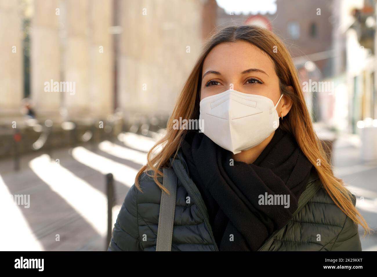 Giovane donna bionda che indossa maschera medica protettiva che cammina in città con abiti invernali Foto Stock