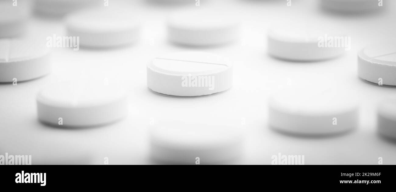 Un mucchio di pillole bianche sparse su uno sfondo bianco luminoso. Messa a fuoco selettiva. Foto Stock