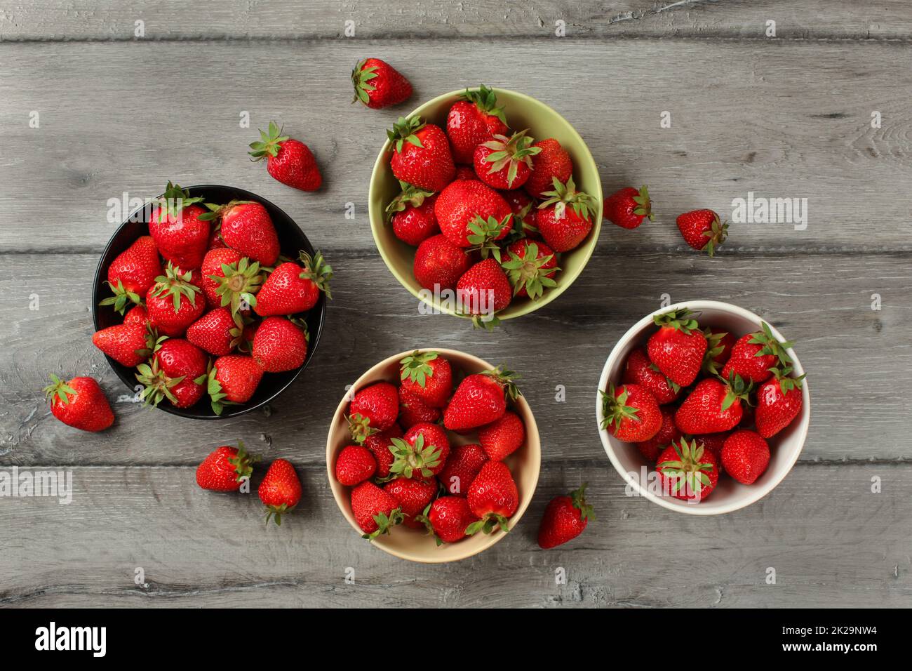 Vista del piano portapaziente - fragole in piccole ciotole di ceramica, alcuni di loro versato sul legno grigio desk. Foto Stock