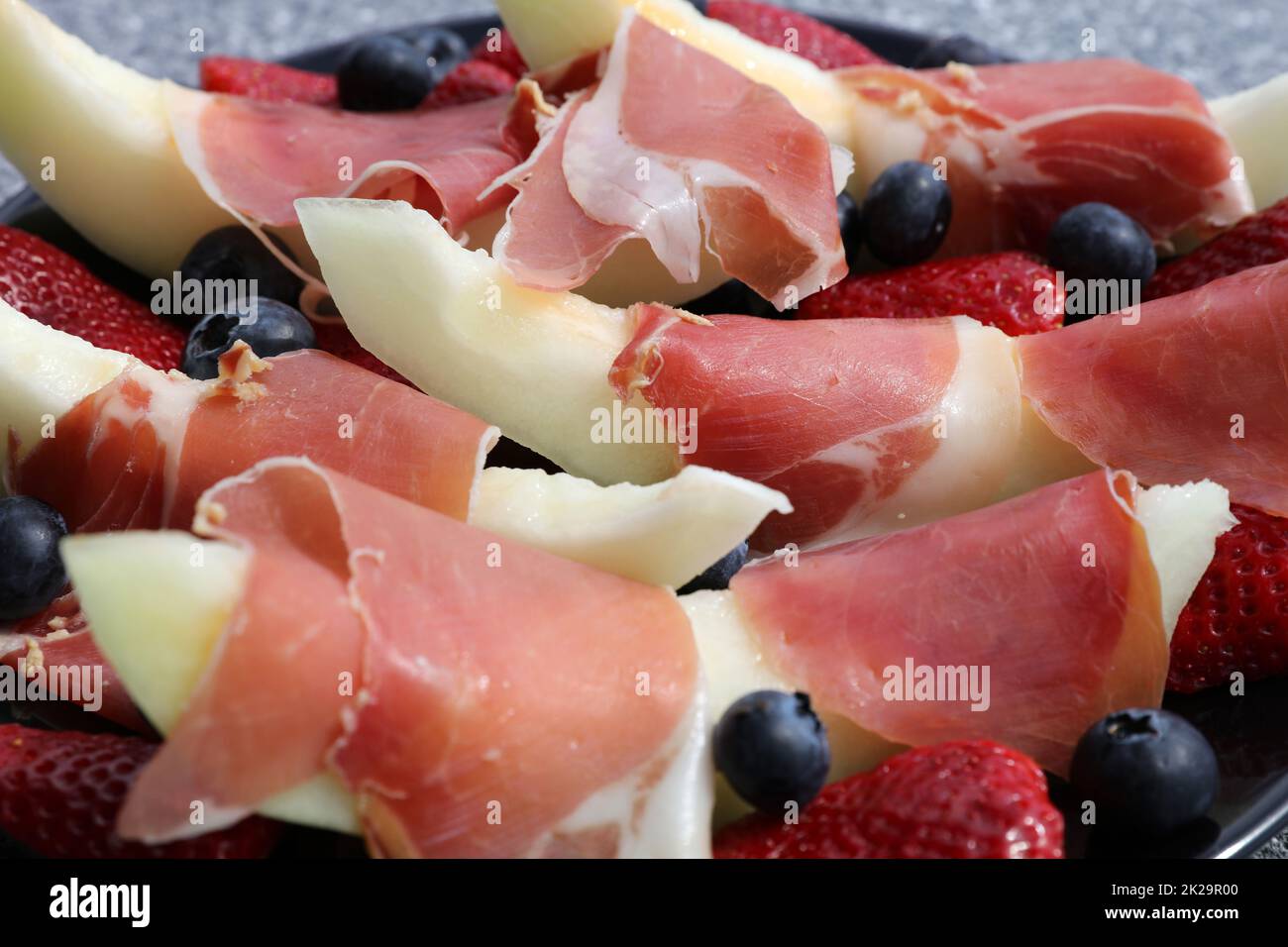 Fettine di melone con prosciutto iberico, fragole e mirtilli Foto Stock
