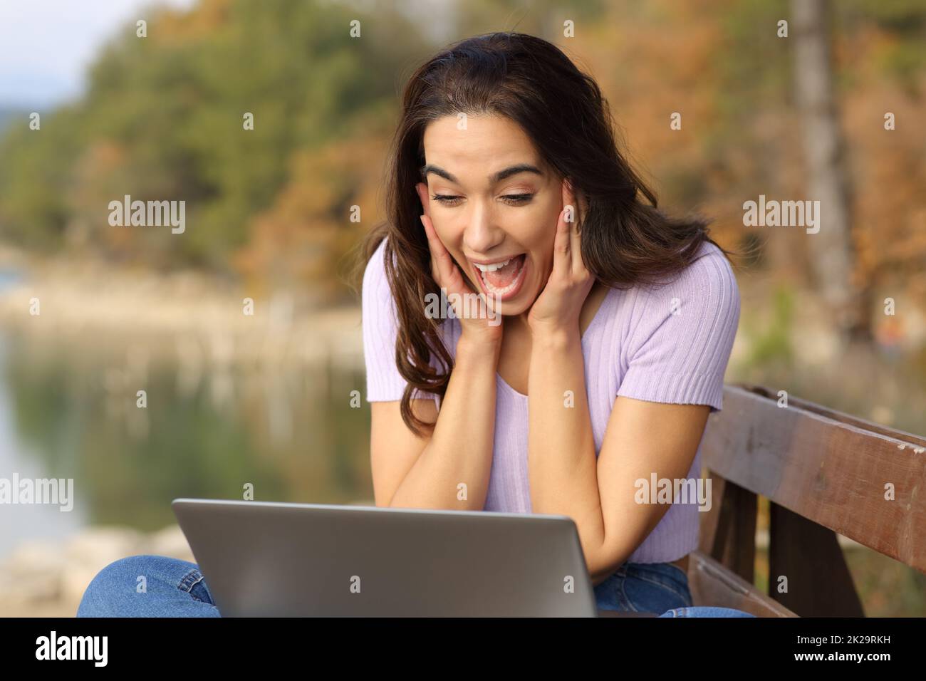 Donna sorpresa che controlla il portatile in un lago in vacanza Foto Stock