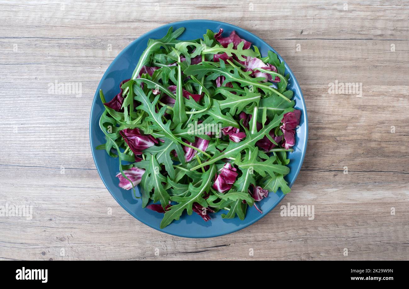 Le foglie di insalata mescolano lo snack verde e succoso, in un piatto su un tavolo di legno Foto Stock