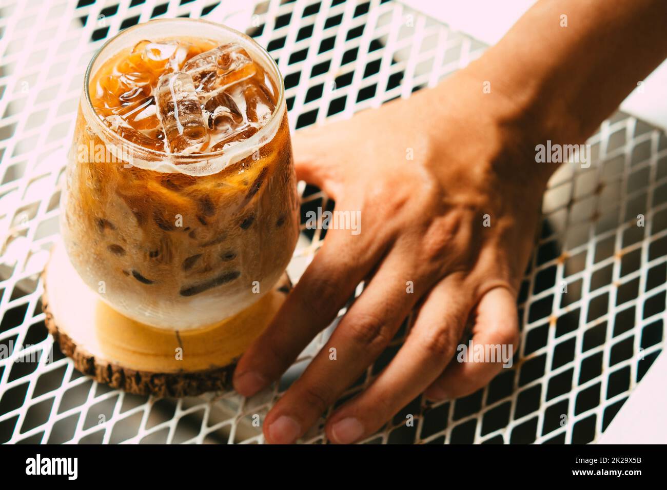 Tenere a mano il caffè latte ghiacciato in un bicchiere con la crema sul fondo. Freddo fondo bevanda estiva Foto Stock