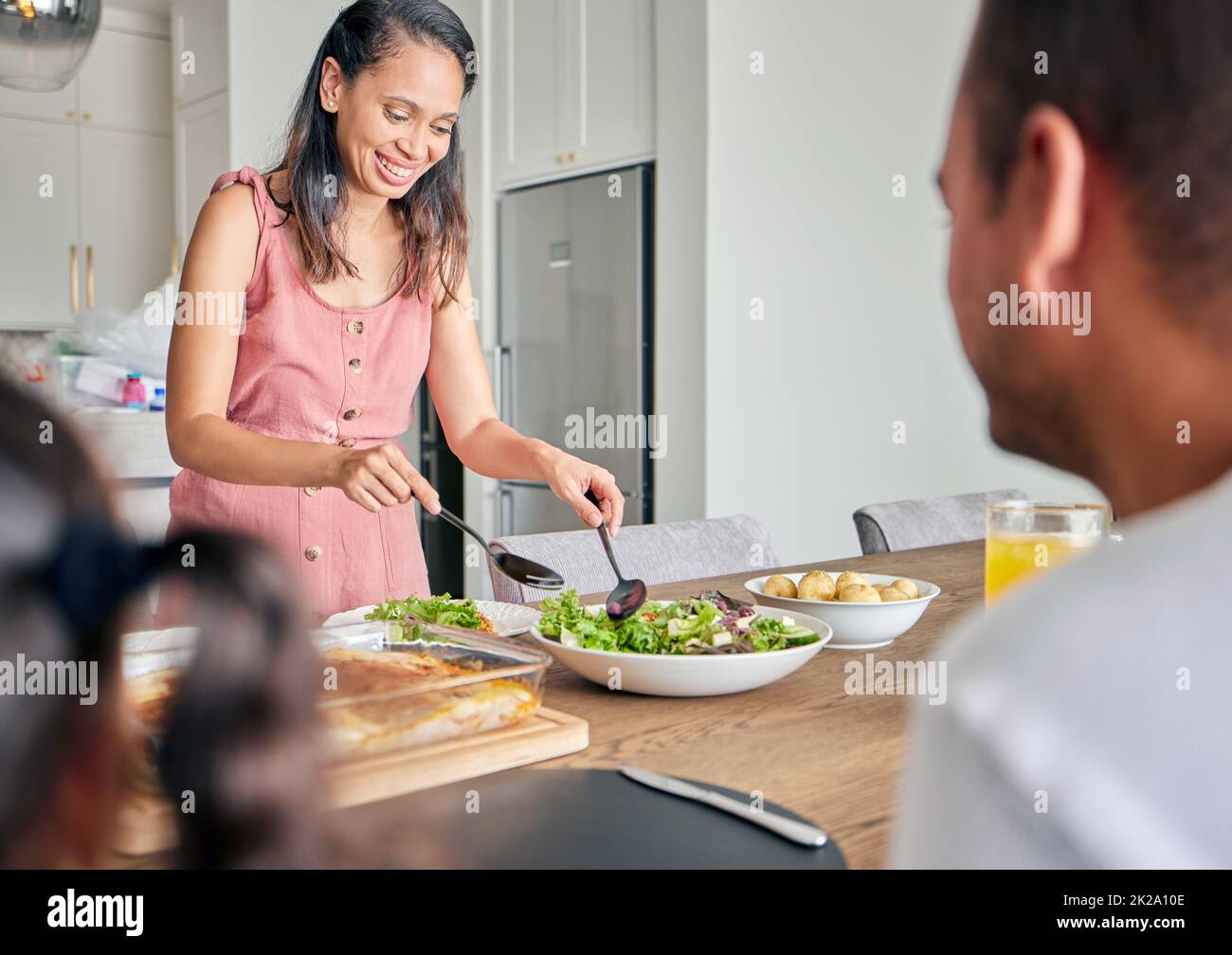 Moglie, mamma e cibo sano con una donna che serve pranzo o cena per la sua famiglia con un sorriso a casa. Casalinga felice che prepara insalata verde e. Foto Stock