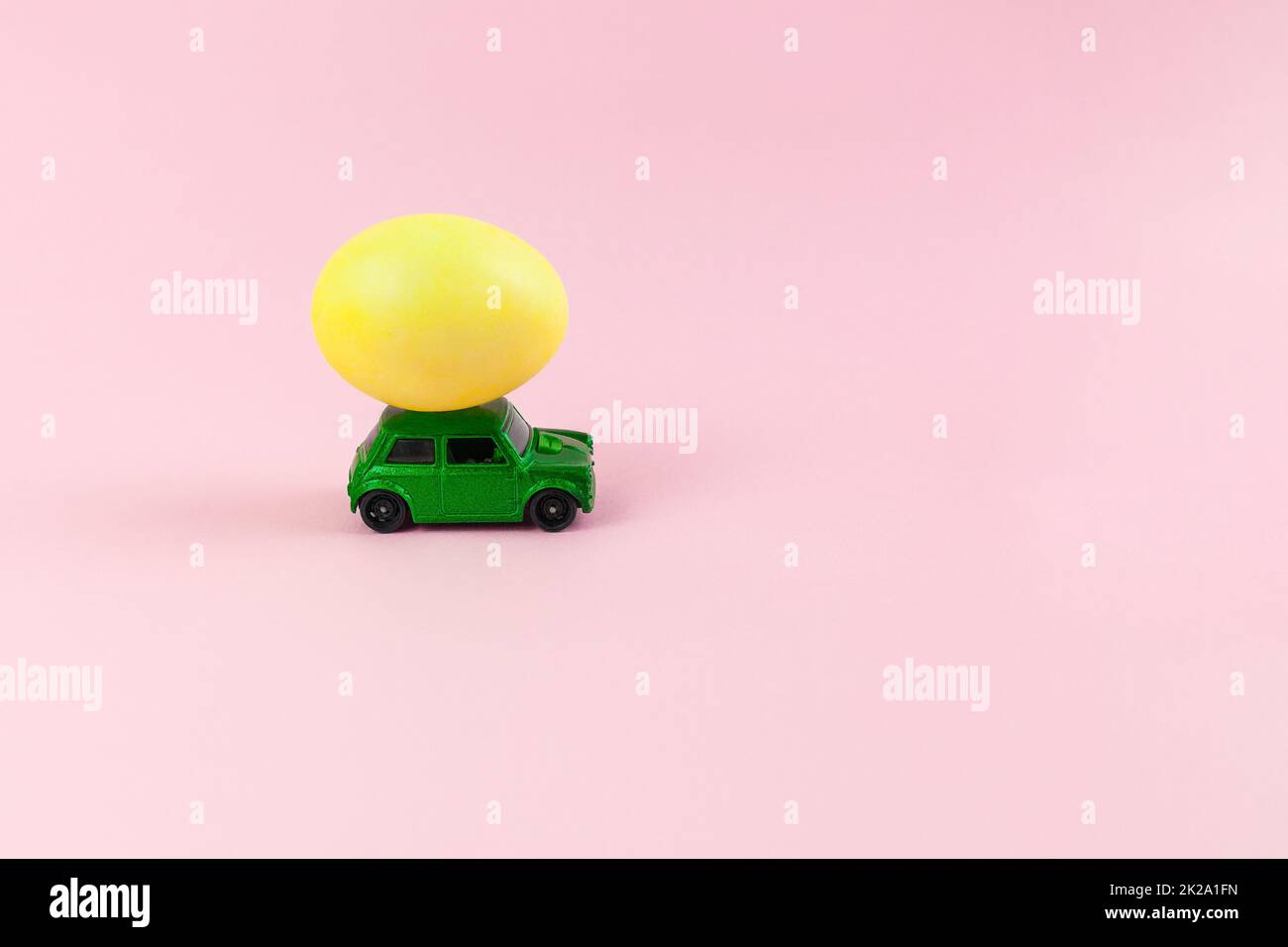 Auto verde giocattolo con uovo di Pasqua sul tetto. Biglietto di Pasqua con spazio per il testo su sfondo rosa. Foto Stock
