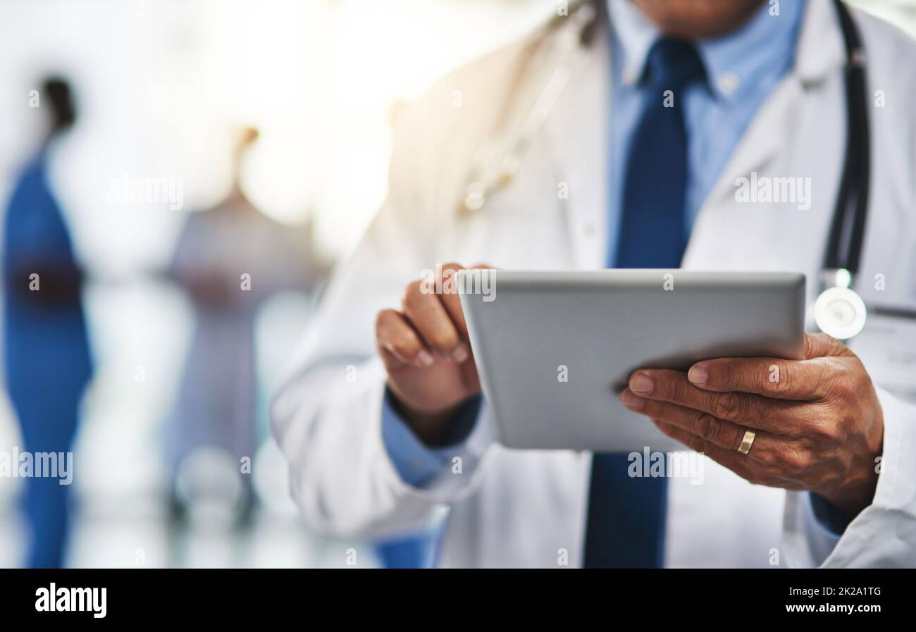 Tenere i pazienti a contatto con lui grazie alla tecnologia wireless. Ripresa ritagliata di un medico utilizzando un tablet digitale con i colleghi sullo sfondo. Foto Stock