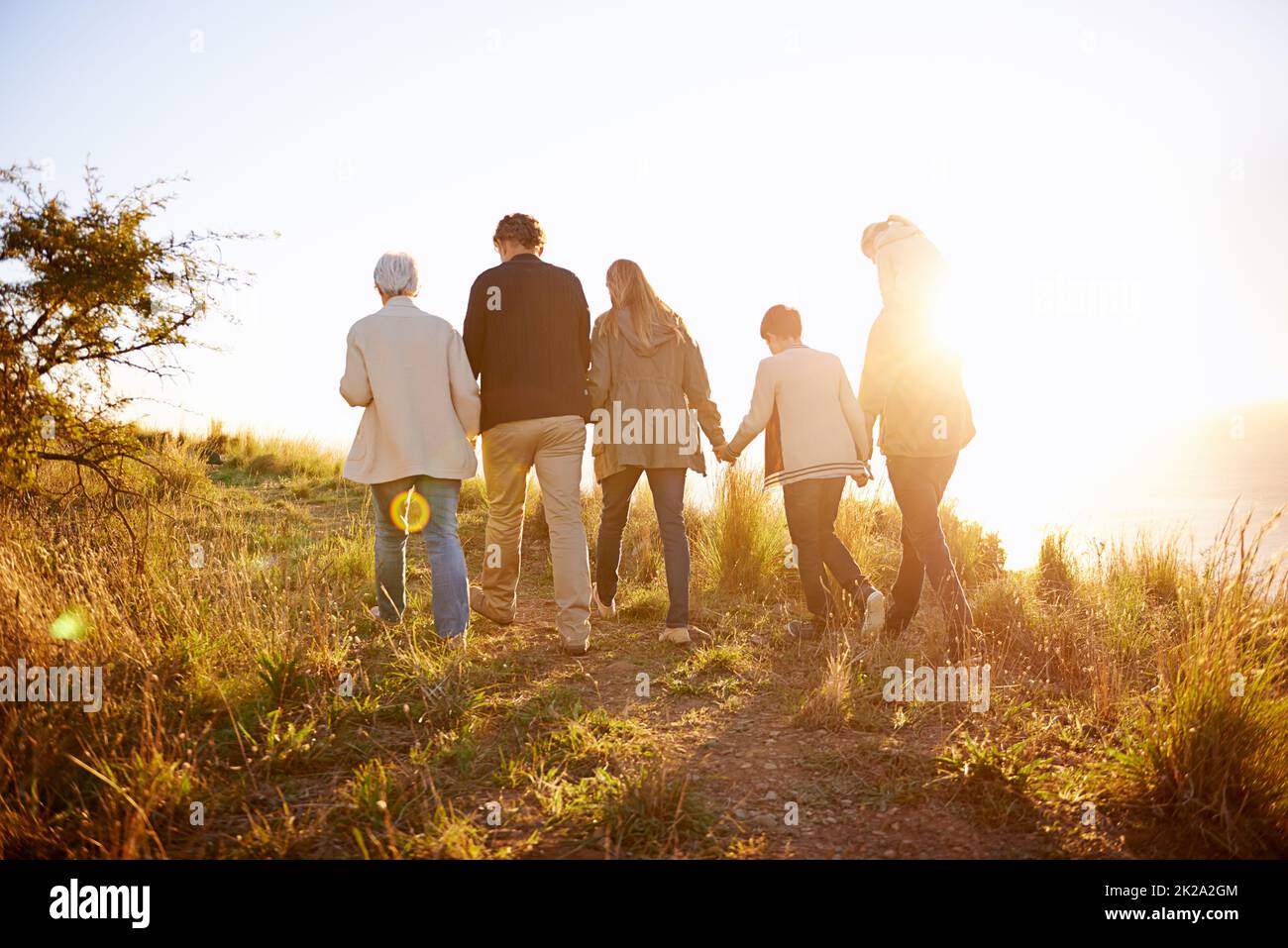 Passeggiando in un pomeriggio d'oro. Foto retrogenerativa di una famiglia multigenerazionale che cammina insieme al tramonto. Foto Stock