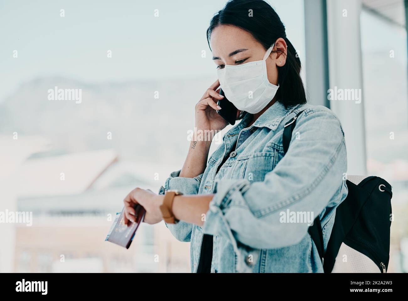 Stiamo esaurendo il tempo per vivere la nostra vita. Scatto di una giovane donna che indossa una maschera, usando uno smartphone e controllando l'ora in un aeroporto. Foto Stock