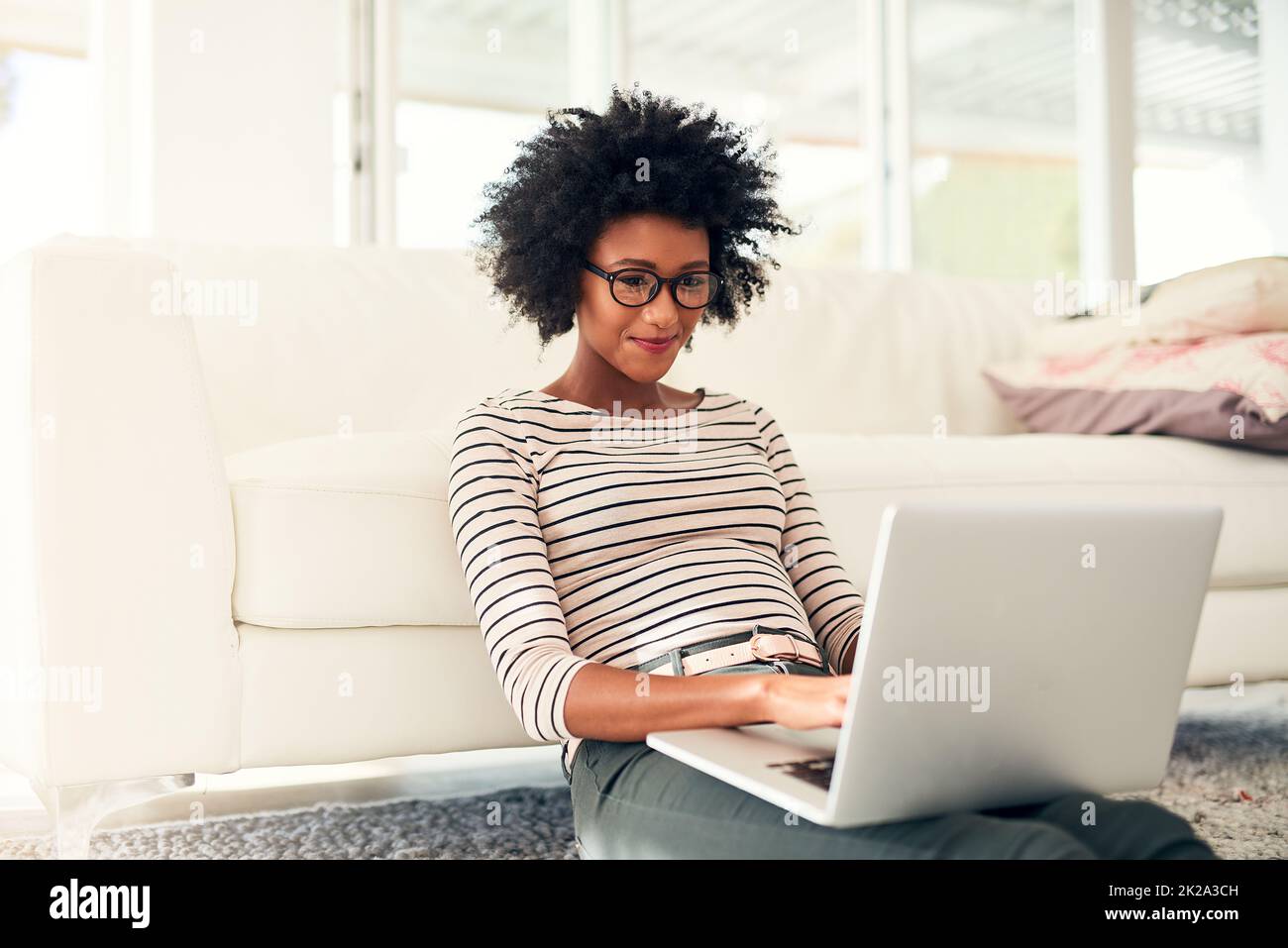 Spendendo un certo del suo tempo libero in linea. Scatto corto di una giovane donna che lavora sul suo laptop a casa. Foto Stock