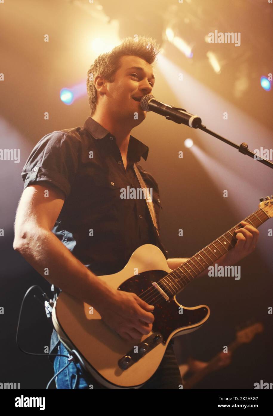 Un giovane esecutore che canta e suona la sua chitarra. Questo concerto è stato creato per l'unico scopo di questo servizio fotografico, con 300 modelli e 3 band dal vivo. Tutte le persone in questo sparo sono modello rilasciato. Foto Stock