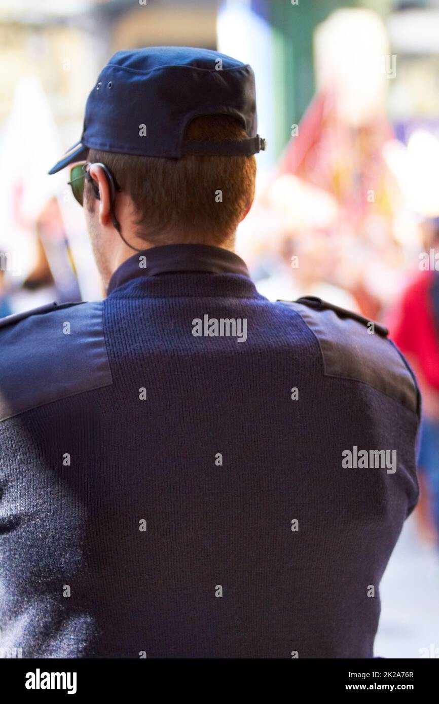 Mantenendolo legale. Dietro l'inquadratura di un poliziotto che tiene sotto controllo un gruppo di manifestanti. Foto Stock