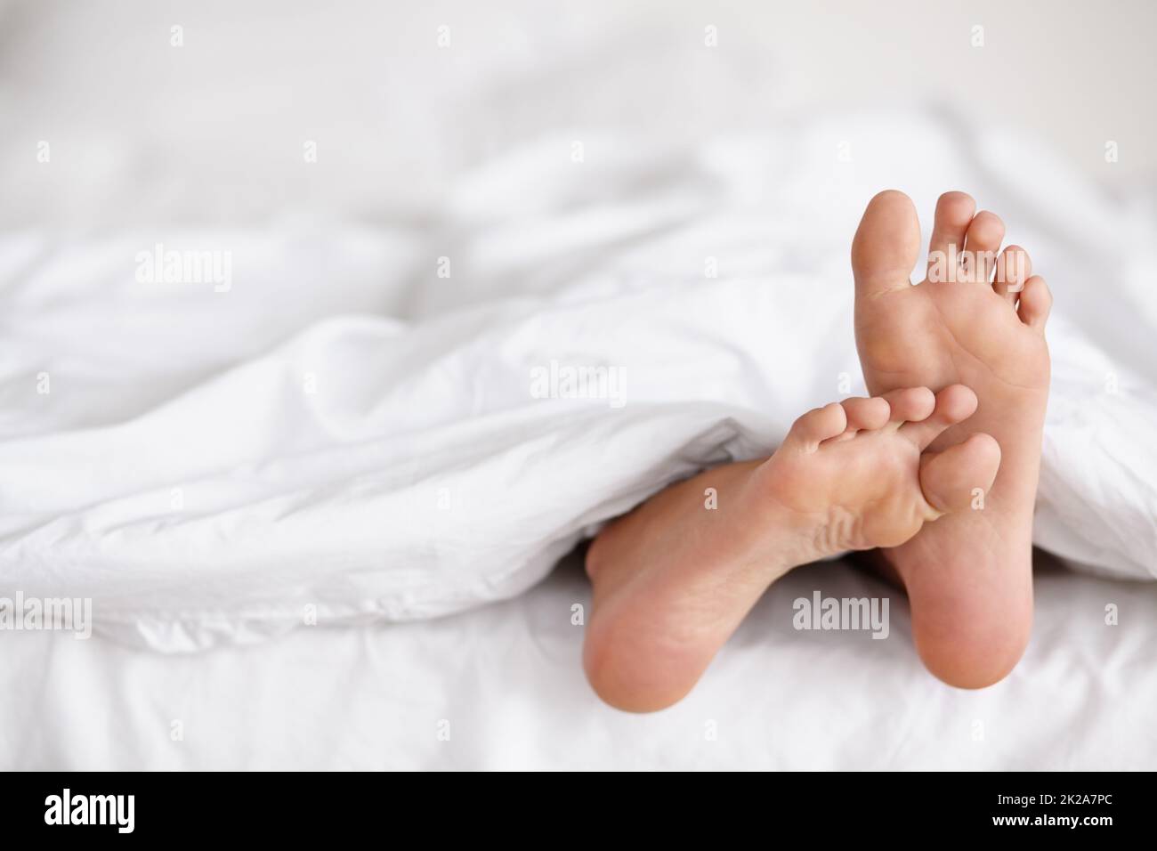 Sguazzare i piedi di veglia. Shot di un paio di piedi di donne che pocano fuori da sotto le lenzuola di un letto. Foto Stock